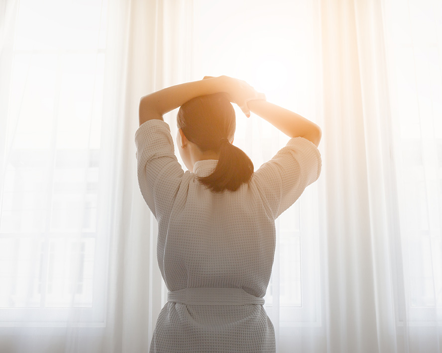 Woman dealing with chronic illness stretching in the window. Therapy and support for chronic or life-altering illness.